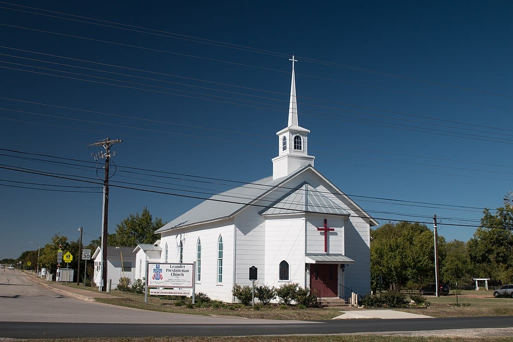 White church with steeple and red cross sign.