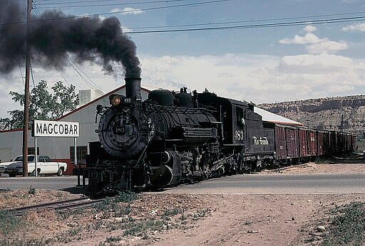 Steam train near industrial building with Magcobar sign.