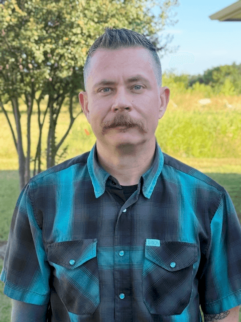 Man with mustache wearing plaid shirt outdoors