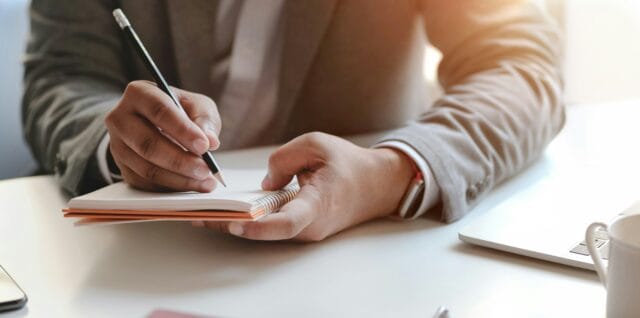 Businessperson writing notes in notebook at desk