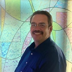 Smiling man in blue shirt before stained glass