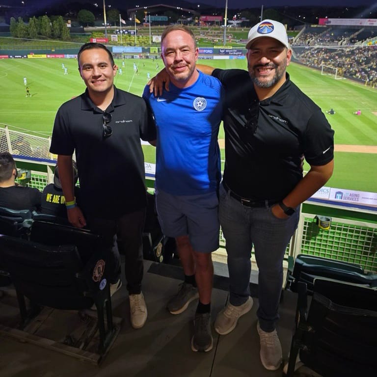 Three friends posing at a soccer stadium.
